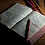 An open Bible on a wooden table accompanied by colored pencils, symbolizing study and spirituality.